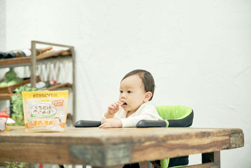 椅子に座っておこめぼーを食べる赤ちゃん