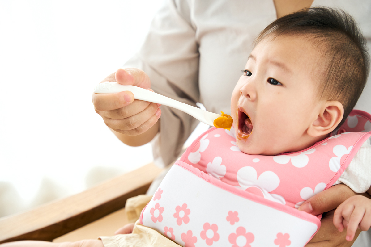 離乳食の開始は遅くするべき？：お母さんに離乳食を食べさせてもらっている赤ちゃん