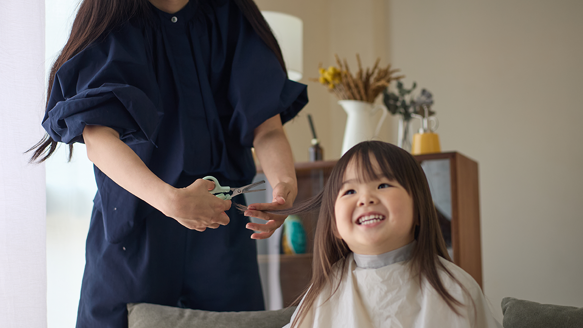 おうちでのセルフカット中に笑顔を見せる子どもと襟足の髪を少しずつ散髪する様子